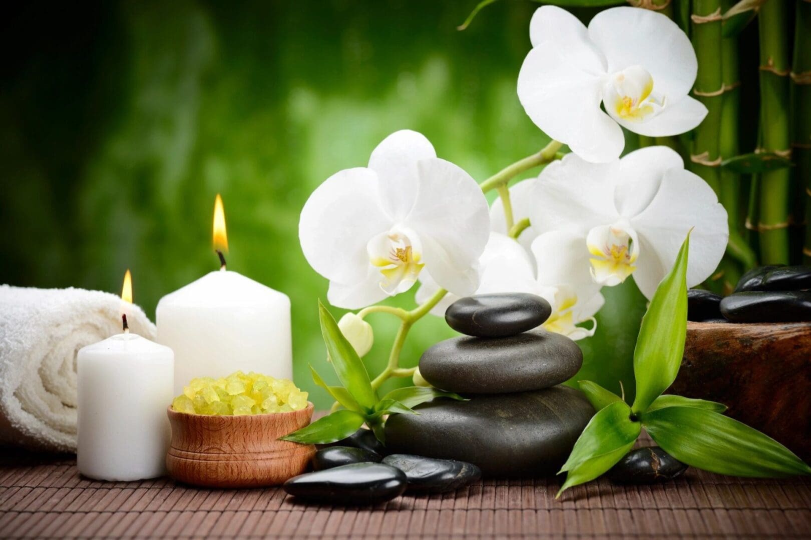 A candle, rocks and flowers on the table.