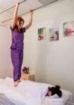 A woman in purple scrubs standing on top of a bed.